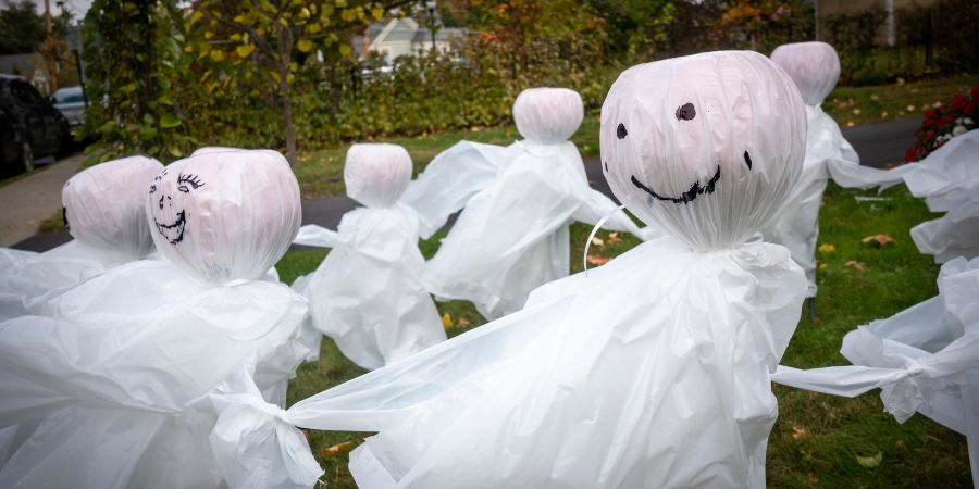 DIY Halloween decorations for outside with homemade ghost figures made from white plastic and drawn-on faces arranged in a front yard.
