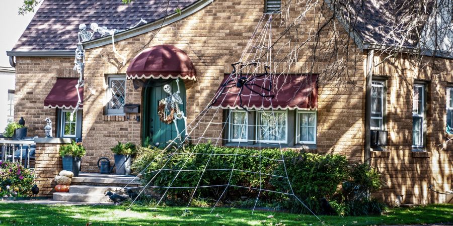Best Halloween yard decorations with giant spider webs, skeleton figures, and spooky accents covering the front of a brick house.