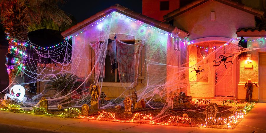Best outdoor Halloween decorations with giant spider webs, glowing lights, tombstones, and spooky props covering the front yard of a house.