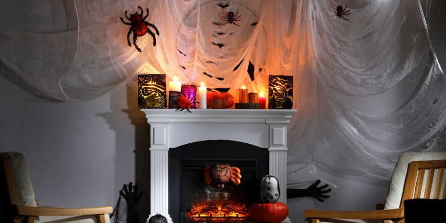 Halloween interior design with spooky cobwebs, spiders, glowing candles, and pumpkins decorating a living room fireplace for a haunted look.