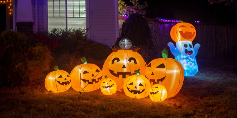 Cool Halloween decorations with glowing inflatable jack-o’-lanterns and a cheerful ghost creating a fun and festive front yard display.