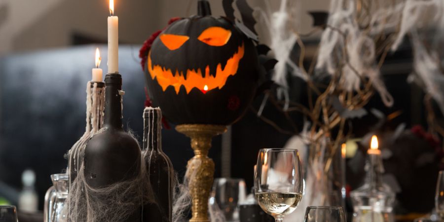 "Halloween decoration ideas for a spooky dining setup with a black jack-o’-lantern centerpiece, cobweb candles, and eerie table accents.