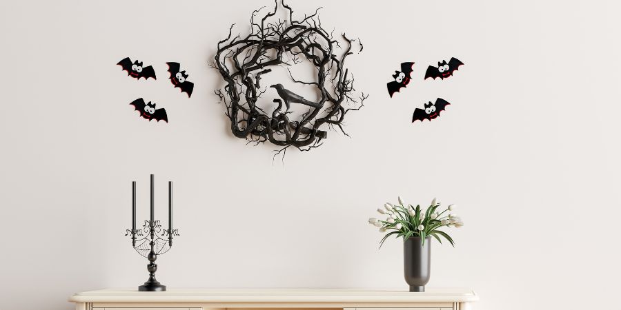 "Halloween interior decorating with a spooky black wreath, bat wall decals, and gothic candle holders creating a simple yet festive display.