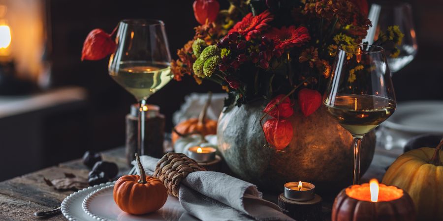 "Halloween decoration ideas for a cozy dining table with pumpkins, candles, autumn flowers, and wine glasses creating a festive seasonal atmosphere.