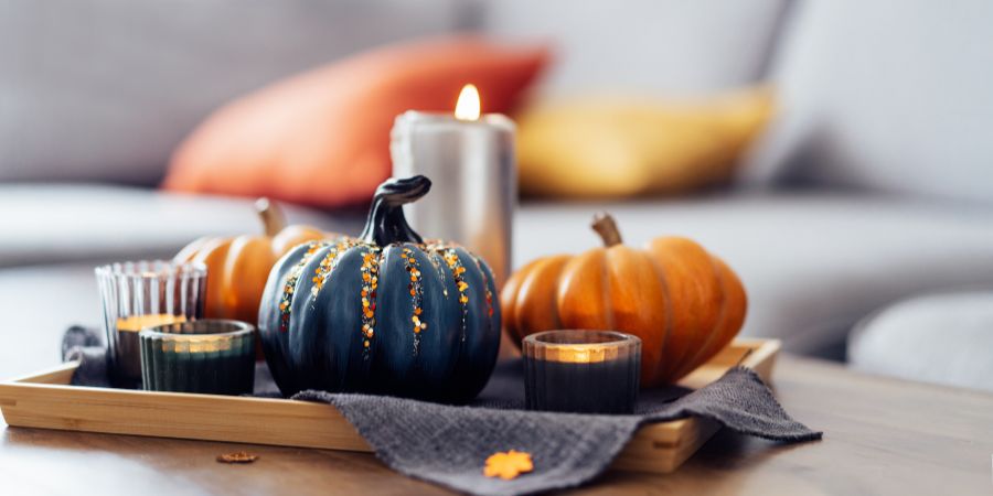 Halloween home decor with a tray of candles, orange pumpkins, and a black painted pumpkin centerpiece creating cozy seasonal style in a modern living room.