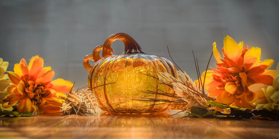 Unique Halloween decorations with a glass pumpkin centerpiece surrounded by bright orange and yellow autumn flowers on a wooden table.