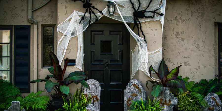 Over the top Halloween decorations with giant spiders, creepy cobwebs, and tombstones creating a haunted front yard scene.