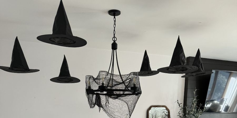 Halloween interior decorating with floating black witch hats and a chandelier draped in spooky fabric for a magical haunted house look.