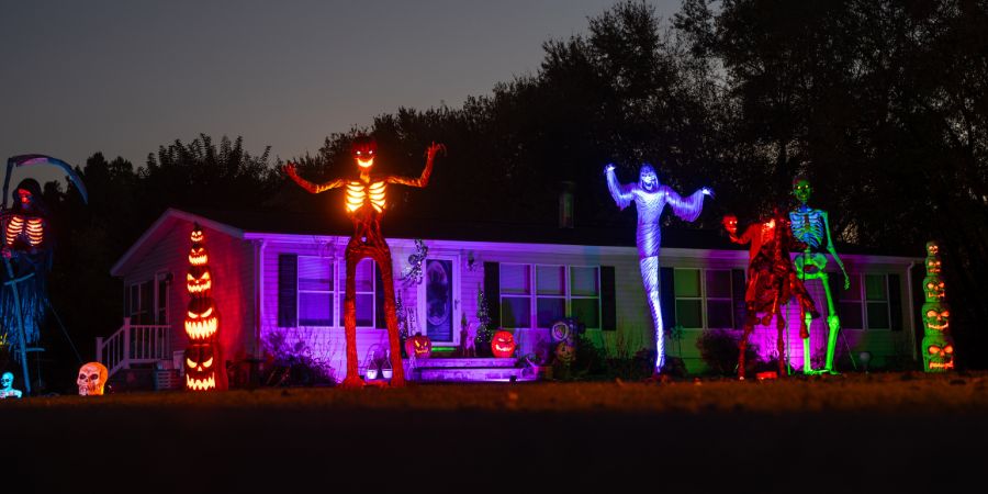 Over the top Halloween decorations with glowing skeletons, spooky figures, and colorful lights creating a dramatic haunted yard display.