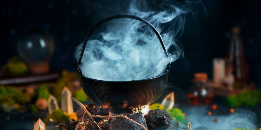 Unique Halloween decorations with a smoky black witch cauldron surrounded by crystals, moss, and potion bottles for a mystical display.