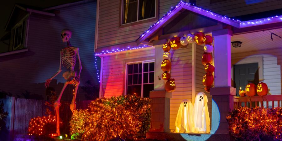 Best Halloween yard decorations with a towering skeleton, glowing jack-o’-lantern arch, and illuminated ghost figures on a festive front porch.