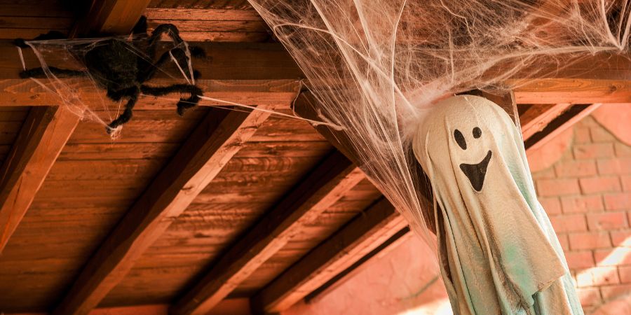 Homemade Halloween decorations indoors and outdoors with a hanging ghost figure and giant spider in cobwebs on a wooden ceiling.