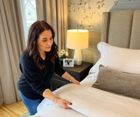 Interior designer & QC design School graduate, Niki Panagiotopoulos, arranging bedding in a modern bedroom featured in an interior design portfolio example, showcasing professional styling and attention to detail.