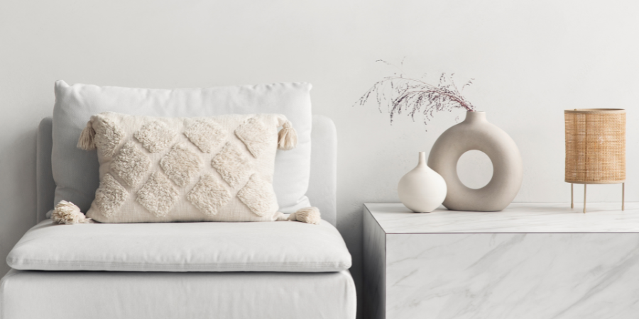 Neutral minimalist living room design with white sofa, textured pillow, ceramic vases, and marble side table.
