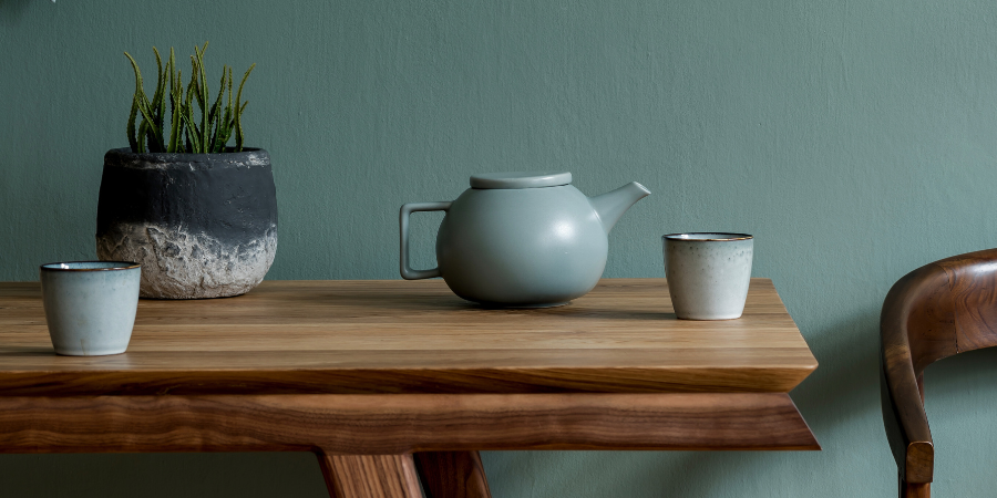 Minimalist dining or tea table with ceramic teapot, cups, potted plant, and natural wood textures.