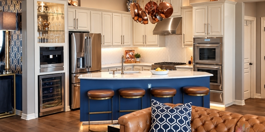 A kitchen showcasing a prominent blue island with white countertops and four round brown leather barstools, surrounded by cream-colored cabinets, stainless steel appliances, a built-in wine fridge, and hanging copper pots, with a brown tufted leather sofa visible in the foreground.