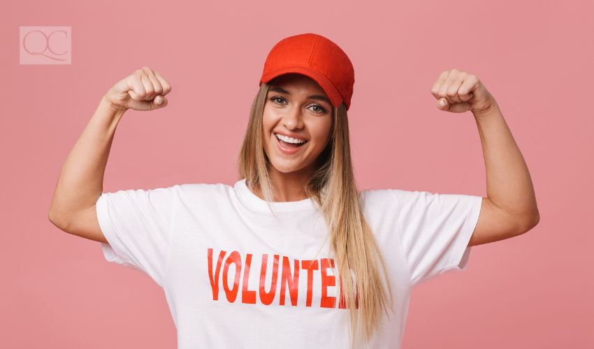 Happy young volunteer girl standing isolated over pink background, flexing biceps