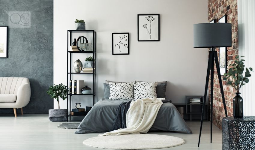 Vase on metal table and grey lamp in spacious bedroom with white carpet and gallery on wall above bed, mixing textures concept