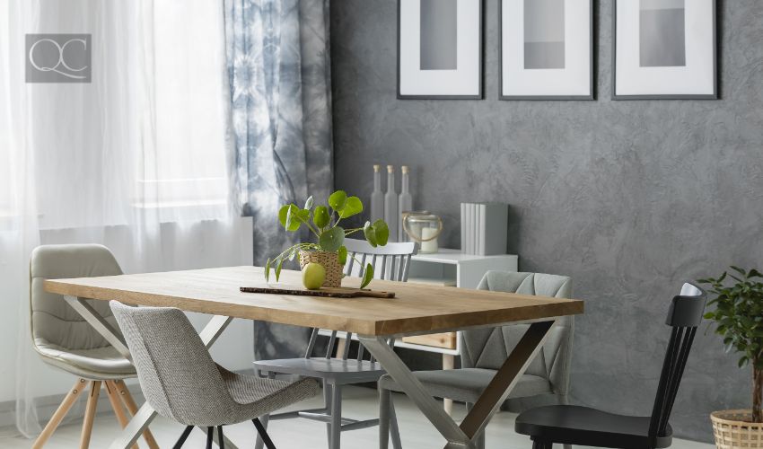 Plant and apple on wooden table with chairs in cozy dining room with paintings on grey wall above cupboard, monochromatic color trend