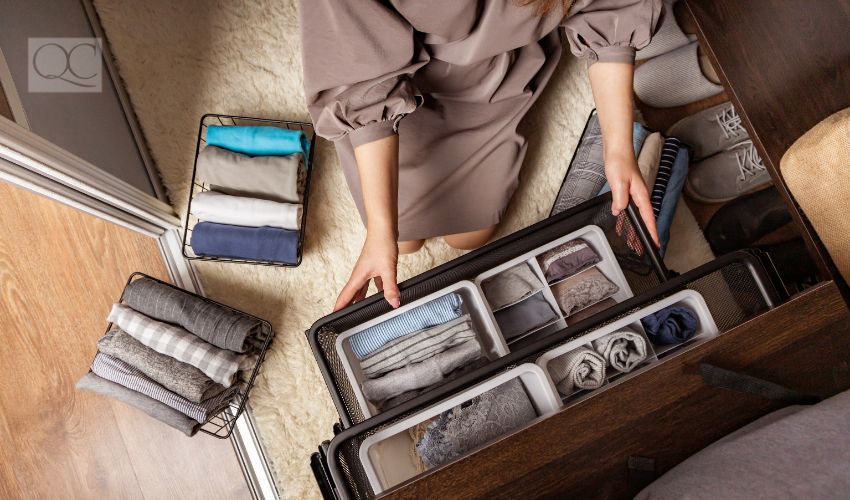 Woman's hands with neatly put underwear, clothes and accessories modern wardrobe organization top view. Woman arms carrying ecological minimalist clothing box container storage Marie Kondo method