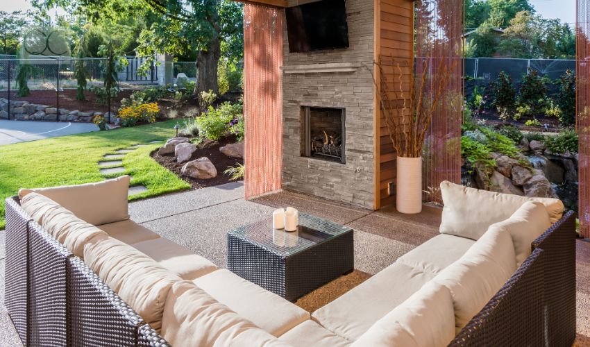 Beautiful covered patio with television, fireplace, and couch, behind new luxury home