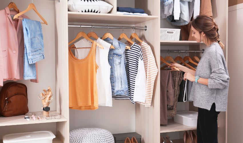 Woman choosing outfit from large wardrobe closet with stylish clothes, shoes and home stuff. Professional organizing.