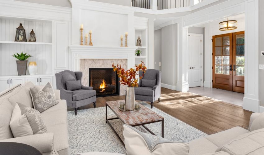 Beautiful living room in new traditional style luxury home. Features vaulted ceilings, fireplace with roaring fire, and elegant furnishings. Shows foyer front door. Interior design apps article.