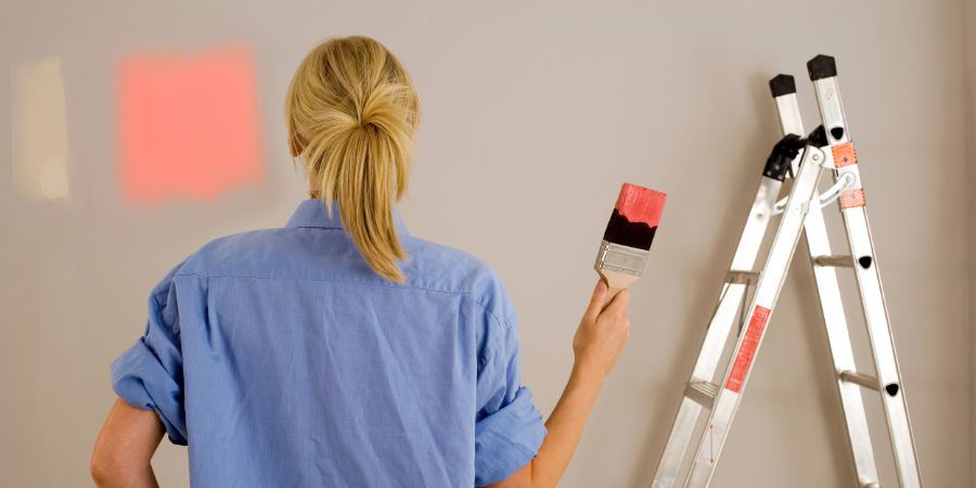 Diy woman decorating at home painting wall with test swatches holding paintbrush dipped in red paint. Color consultant article.