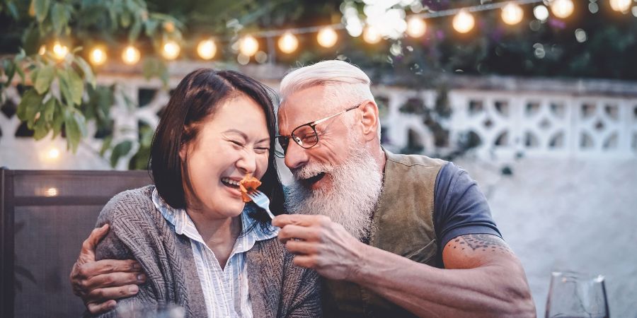 Happy senior couple having fun at dinner house party - Older people with different ethnicity doing a romantic date for celebrating anniversary - Elderly, food, drink and love concept. Aging in Place article.