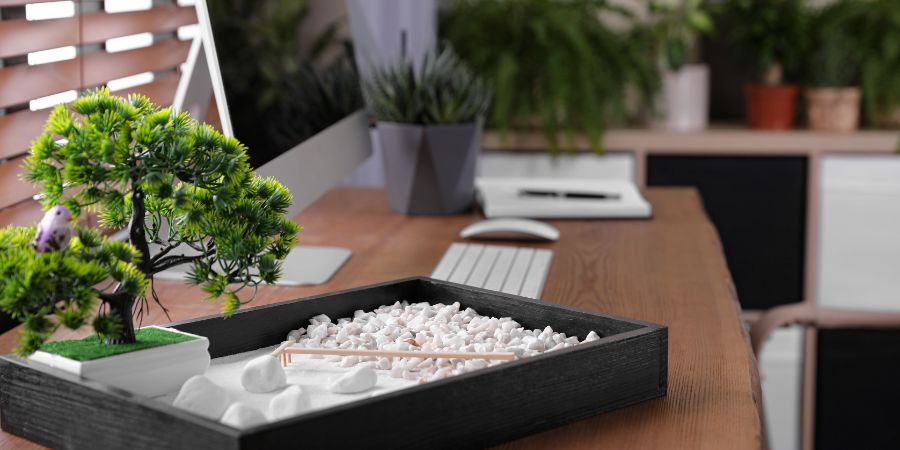 Beautiful miniature zen garden and computer on wooden table in office. Feng Shui article.