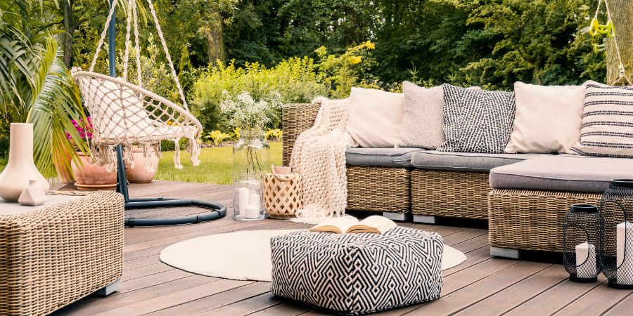 Book on a black and white pouf in the middle of a bright terrace with a rattan corner sofa, hanging chair and round rug. Real photo. Landscape design article.
