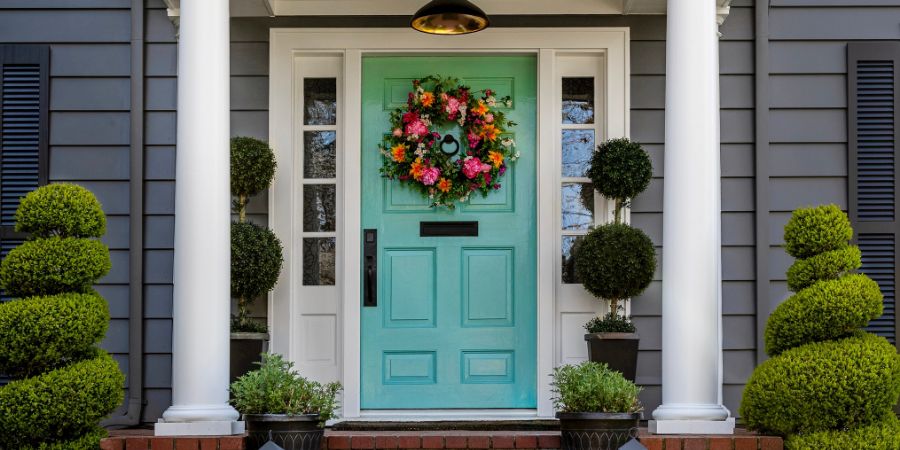 Beautifully decorated turquoise colored front door of traditional home. Brick path and trimmed hedges. Landscape design article.