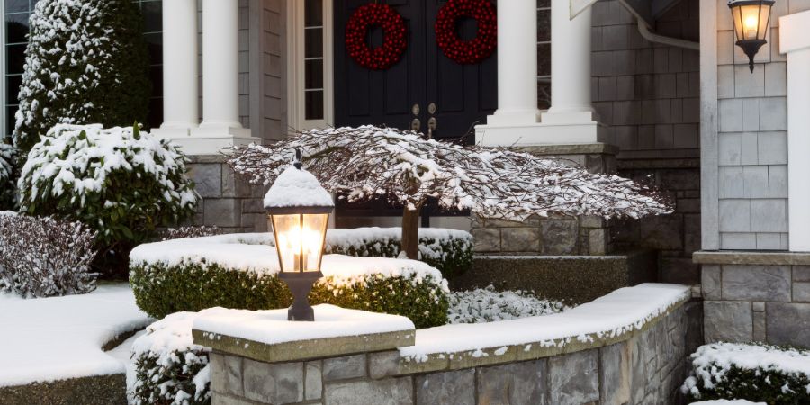 Closeup photo of home entrance during the holidays with fresh snow. Landscape design tips article.