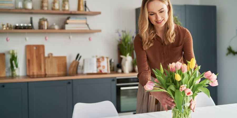 Caucasian woman putting fresh tulips into the vase. Home staging article.