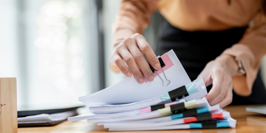 Businesswoman hands working in Stacks of paper files for searching and checking unfinished document achieves on folders papers at busy work desk office. Professional organizers article.