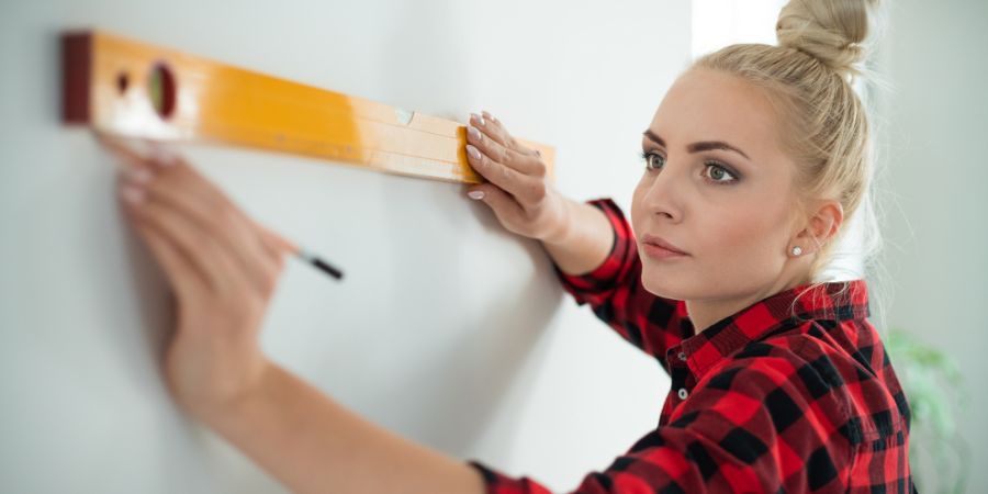 Indoor shot of young woman using leveling tool at home. Close up of face. Home design. Business insurance article.