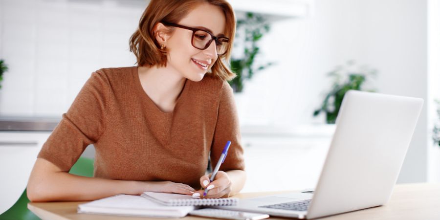Woman on remote work or online education, using laptop computer, making notes, indoors at office or home at daytime. Online business, young professional at workplace. Working from home. First 6 months of business article.
